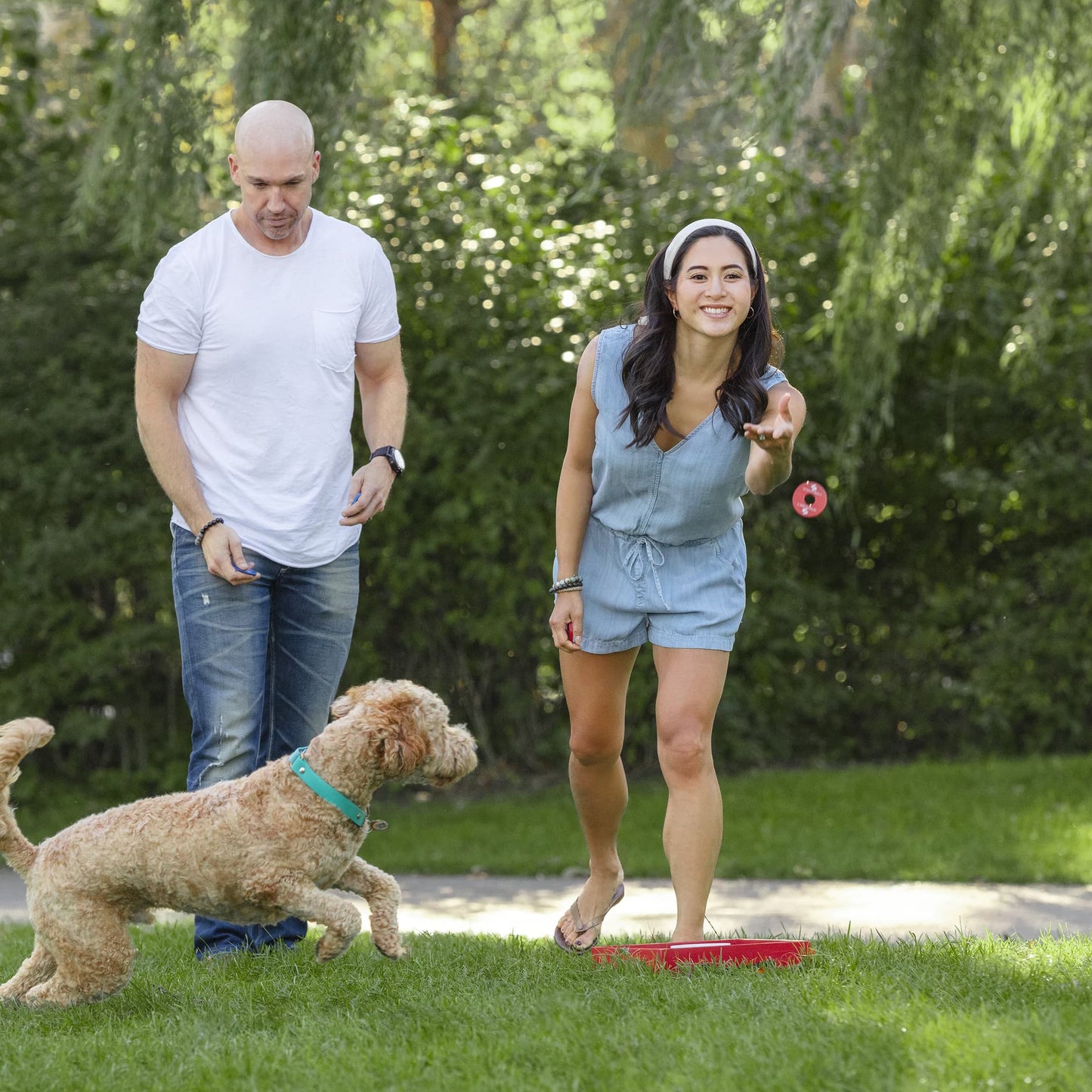 Sportcraft Wooden Washer Toss Game - Lifestyle Image - Woman & Man playing the game, Dog chasing washer