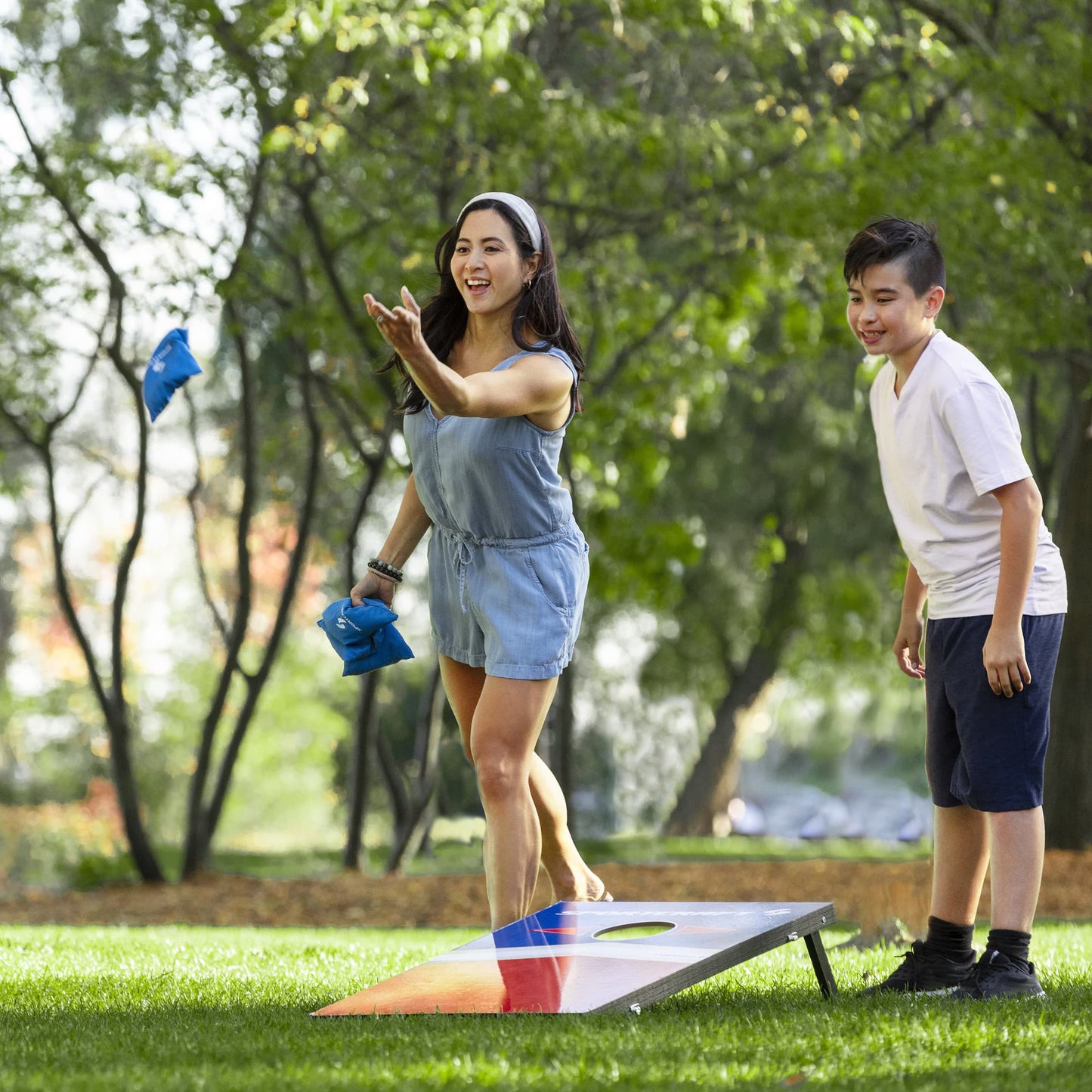 Sportcraft Wooden Corn Hole Bean Bag Toss Lifestyle Image, Woman throwing blue bean bag at target with son watching